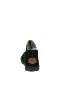 Botines de ante negros con un suave forro de piel gris, que presentan una etiqueta de cuero marrón y una suela de goma. La vista trasera muestra un acento de costura.