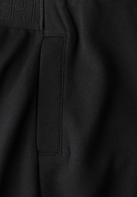 Shorts de sport noirs avec une texture lisse, une pochette à rabat et des lettres en relief, dotés de coutures plates pour un design épuré.