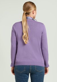 Fioletowy sweter wykonany na drutach z okrągłym dekoltem i długimi rękawami, z prążkowanymi mankietami i luźnym krojem, połączony z niebieskimi dżinsami.