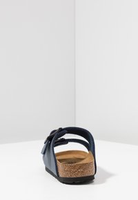 Mörkblå sandal med öppen bak, justerbar rem, korkfotbädd och sträv gummisula. Minimalistisk design utan framträdande mönster.