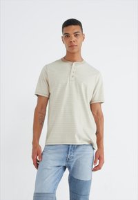 Svetlobežový krátky rukáv henley tričko s horizontálnymi prúžkami, so zapínaním na tri gombíky a hladkou, jemnou textúrou, skombinované s modrými denovým džínami.