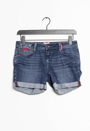Mørkeblå denimshorts med opklappede manchetter hængende på en sort bøjle mod en hvid baggrund.