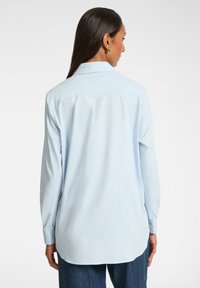 Camisa abotonada de color azul claro con mangas largas, cuello puntiagudo y un dobladillo trasero más largo. Hecha de una tela suave con un corte holgado.