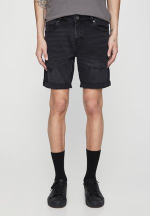 Mustat farkkushortsit, joissa on käännetyt lahkeet, rosoisia yksityiskohtia ja tiukka muotoilu. Yhdistetty mustiin sukkiin ja lenkkareihin.