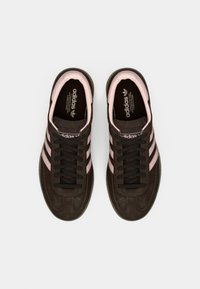 Καφέ σουέτ αθλητικά παπούτσια με ροζ λεπτομέρειες, που διαθέτουν τρεις ρίγες και υφασμένο πάτο. Μαύρα κορδόνια και ενσωματωμένοι πάτοι με λογότυπο ολοκληρώνουν το σχέδιο.