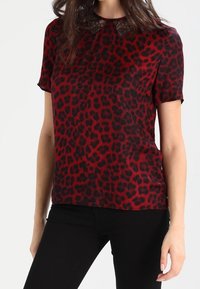 Kortærmet top i rød med sort leopardprint, med en blonde detalje ved halsudskæringen. Blødt stof, almindelig pasform, parret med sorte bukser.