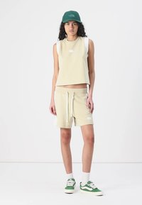 Beige ärmlös topp med logotyp, matchande shorts med sidofickor och grön keps. Kompletteras med gröna och vita sneakers. Av avslappnat tyg.