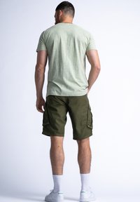 Light green textured t-shirt paired with dark green cargo shorts featuring side pockets. White athletic socks and sneakers complete the look.