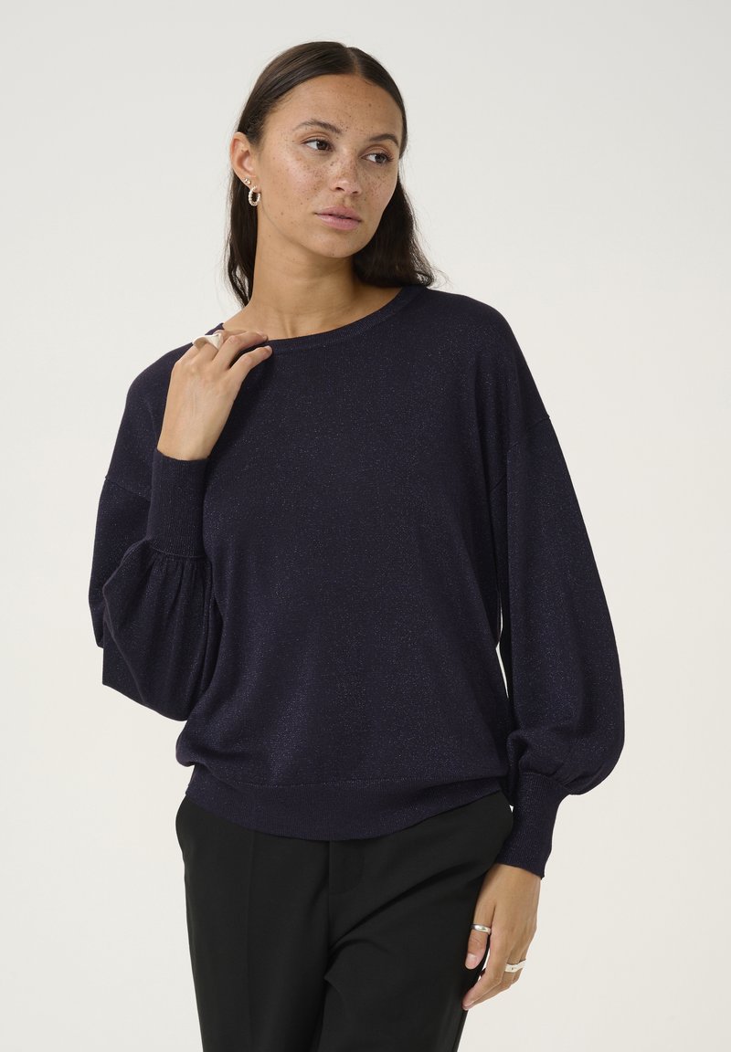 Dunkelblauer Pullover mit lockerem Schnitt, Ballonärmeln und strukturiertem Finish. Kombiniert mit schwarzen Hosen.