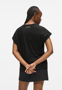 Fekete, rövid ujjú pamut póló, kerek nyakkivágással és egy apró fehér logóval a hátán. Egyszerű, laza dizájn.