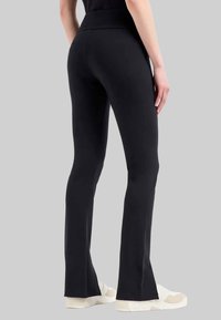 Zwarte yoga-broeken met een hoge tailleband, uitlopende pijpen en een gladde textuur, gecombineerd met witte sportschoenen.