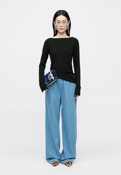 Juodas ilgomis rankovėmis marškinėlis, laisvi šviesiai mėlyni džinsai ir raštuoti leopardų odiniai batai. Laiko mėlyną šventinį delninį su dekoratyviais akcentais.