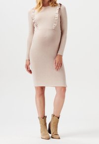 Robe à manches longues, longueur genou, en tissu beige doux avec des accents volantés le long de l'encolure. Associée à des bottes de cow-boy en tan.