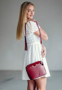 Červená kožená kabelka přes rameno s elegantním designem, stříbrnými akcenty a řetízkovým popruhem. Obsahuje zipové zapínání a má strukturovaný tvar.