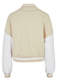 Krátký svetřík v béžové barvě s bílými rukávy. Má kulatý límec, žebrované manžety a proužky na lemu pro zvýraznění detailů. Měkká textura.