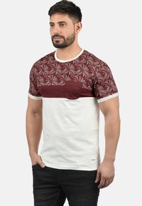 Short-sleeve T-shirt featuring a maroon patterned upper section and white lower half. Includes a chest pocket and contrasting neck trim.