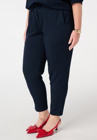 Pantalons de jogging navy en tissu textur�é, avec une taille à cordon de serrage et des poches latérales. Associés à des talons rouges brillants avec un détail en nœud.