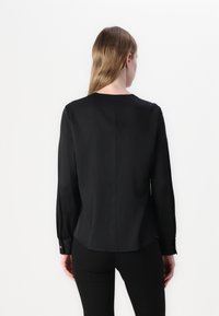 Blusa nera a maniche lunghe con texture liscia, scollatura rotonda e piccoli dettagli con bottoni sui polsini, caratterizzata da un orlo leggermente curvato.