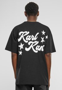 Black cotton t-shirt featuring bold white "Karl Kan" text and star graphics on the back. Short sleeves and relaxed fit design.
