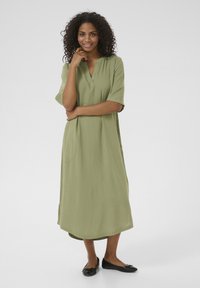 Robe vert olive, longueur genou, avec des manches courtes, décolleté en V et poches latérales. Tissu lisse avec une coupe décontractée et une texture subtile.
