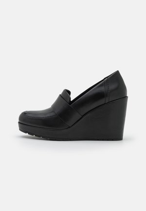 Zapatos de cuña de cuero negro con punta redonda y una banda en la parte frontal. Suela texturizada para mayor agarre. Diseño elegante y moderno.