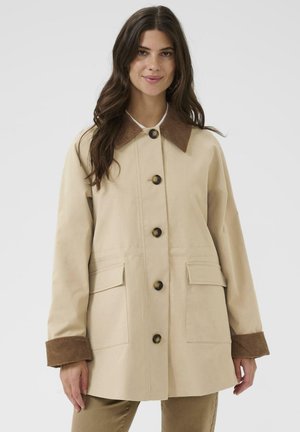 Beige yderjakke med en fløjlsagtig krave, brune knapper, to forlommer og et afslappet design. Lange ærmer med ribstrikkede manchetter.
