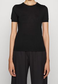 Top negro de manga corta, hecho de un material ligero y suave. Presenta un cuello redondo y una silueta ajustada con una textura sutil.