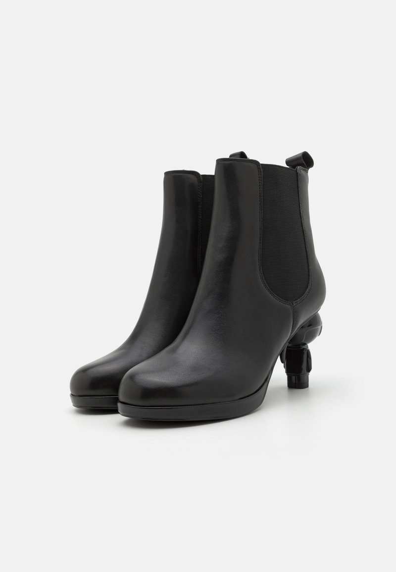 Bottines en cuir noir avec des panneaux latéraux élastiques, bout en amande et un petit talon sculpté. Texture lisse avec un design élégant.