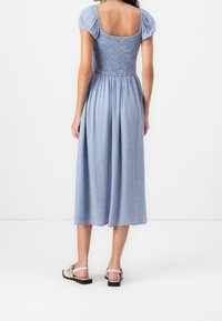 Blå rutig midiklänning med smockad byst, puffärmar och fyrkantig rygg. A-formad silhuett, mjukt tyg, kompletterat med platta sandaler.