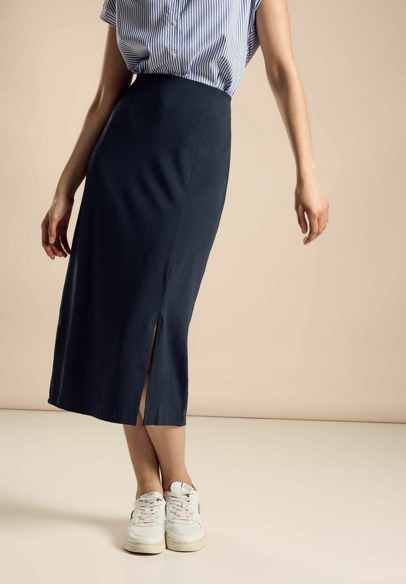 Navy blue mid-length skirt made from a smooth fabric, featuring a side slit. Paired with a striped short-sleeve shirt and white sneakers.