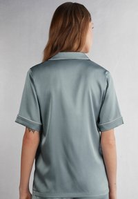 Satin kortärmad skjorta i mjuk grön med vita detaljer. Avslappnad passform och klassisk krage; slät textur och subtil lyster.