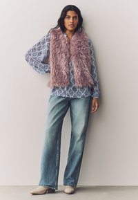 Faux fur vest in soft pink over a blue patterned long-sleeve shirt, paired with light blue wide-leg jeans and beige ankle boots.