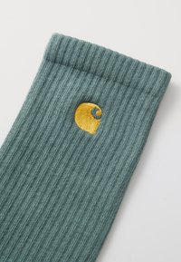 Grüne gerippte Socken mit einem gelben gestickten Logo, aus weichem Material, mit einer strukturierten Optik und einem umgeschlagenen Bündchen.