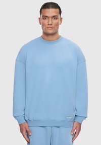 Lyseblå sweatshirt, blødt stof, afslappet pasform, rund hals, ribbede manchetter og kant, har et lille logotag på siden.