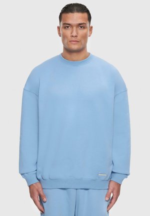 Lyseblå sweatshirt, blødt stof, afslappet pasform, rund hals, ribbede manchetter og kant, har et lille logotag på siden.