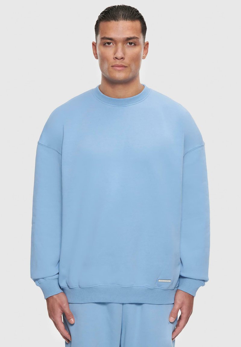 Lyseblå sweatshirt, blødt stof, afslappet pasform, rund hals, ribbede manchetter og kant, har et lille logotag på siden.