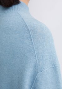 Pulover tricotat de culoare albastru deschis, cu un design cu guler înalt. Textură moale și croială lejeră, cu detalii vizibile ale cusăturilor pe umeri.