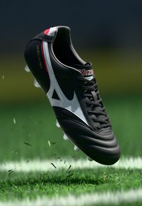 Zwarte voetbalplaat met witte accenten en rode details, voorzien van een glad leren bovenwerk, vetersluiting en gevormde noppen voor grip.