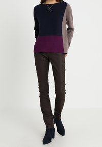 Sweter dzianinowy z kolorowymi blokami w odcieniach niebieskiego, purpurowego i taupe; w połączeniu z dopasowanymi brązowymi spodniami i ciemnoniebieskimi botkami na obcasie.