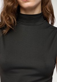 Top senza maniche nera con collo alto, realizzato in un materiale liscio ed elastico con un design aderente e una sottile lucentezza sulla superficie.