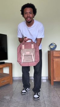 Mochila rosa e bege com alças duplas, tecido texturizado e um bolso frontal. Possui acessórios em metal e alças ajustáveis.