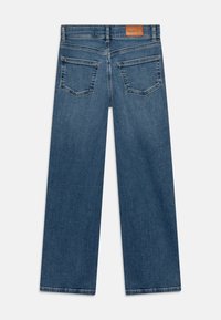 Mėlyni platūs džinsai, rodoma iš nugaros su dviem galinėmis kišenėmis ir rudos odos prekės ženklu ant juosmens.