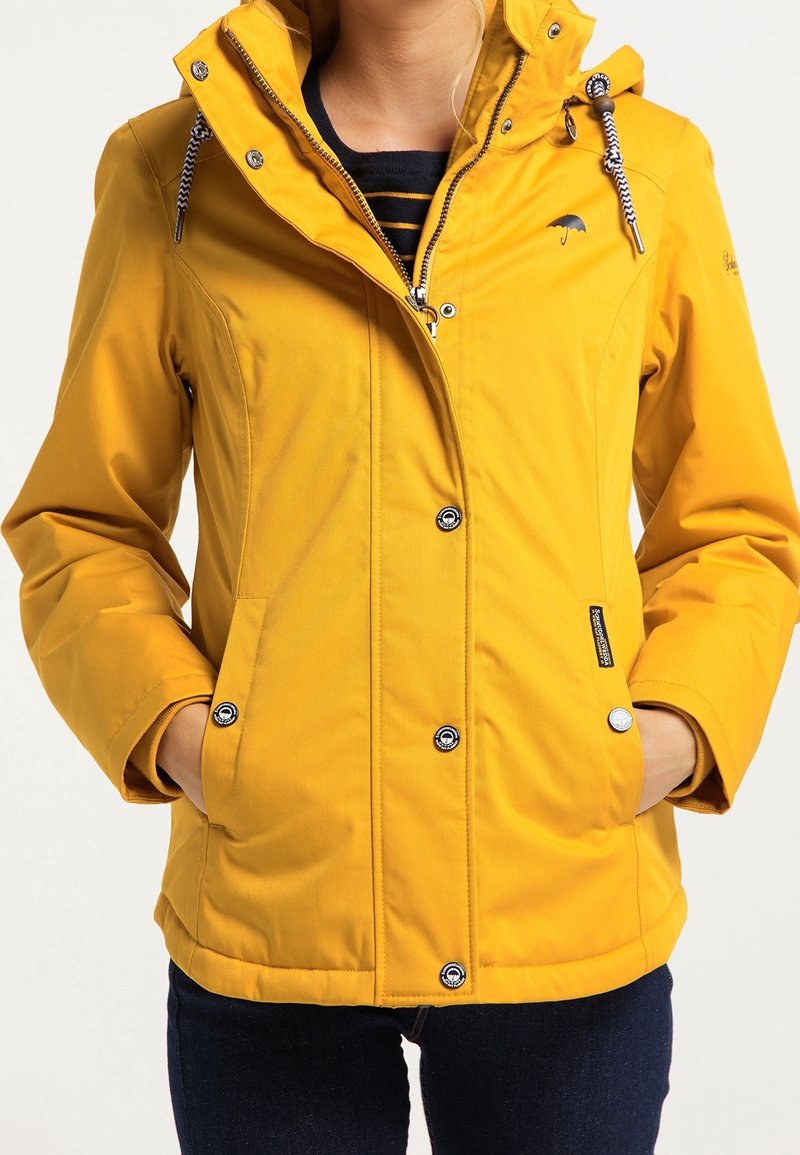 Veste imperméable jaune avec capuche. Dotée de boutons-pression et d'un cordon de serrage autour du cou. Le tissu a une texture lisse et légèrement brillante.