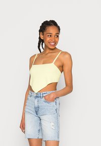 Top crop amarelo claro, texturizado, com decote quadrado e alças finas, combinado com calções de ganga azul claro desgastados.