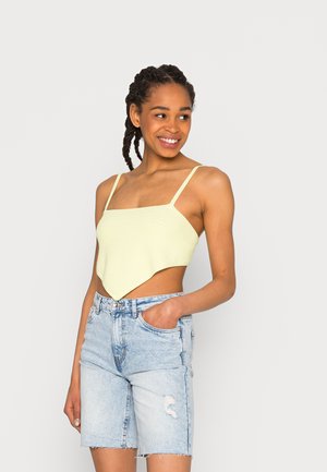 Top crop amarelo claro, texturizado, com decote quadrado e alças finas, combinado com calções de ganga azul claro desgastados.