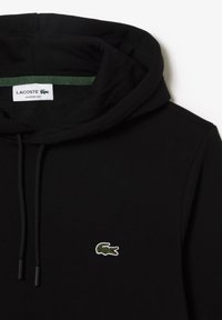 Sweat à capuche noir en coton doux, avec une capuche intérieure verte, des cordons de serrage et un petit logo crocodile brodé sur la poitrine.