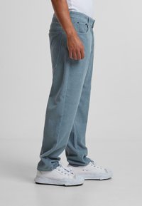 Pantalones de corduroy azul claro con acanalado vertical, corte recto, dos bolsillos y combinados con zapatillas blancas.