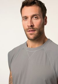 Grijze mouwloze shirt met een ronde halslijn. Beschikt over platte naden en een gladde textuur. Korte pasvorm accentueert de schouders.