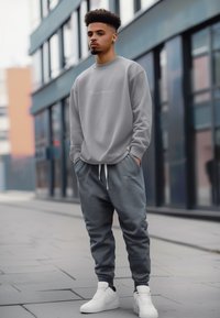 Felpa grigia e pantaloni jogger abbinati con polsini elastici, con un accento del logo. Indossati con sneakers bianche, sullo sfondo di un ambiente urbano.
