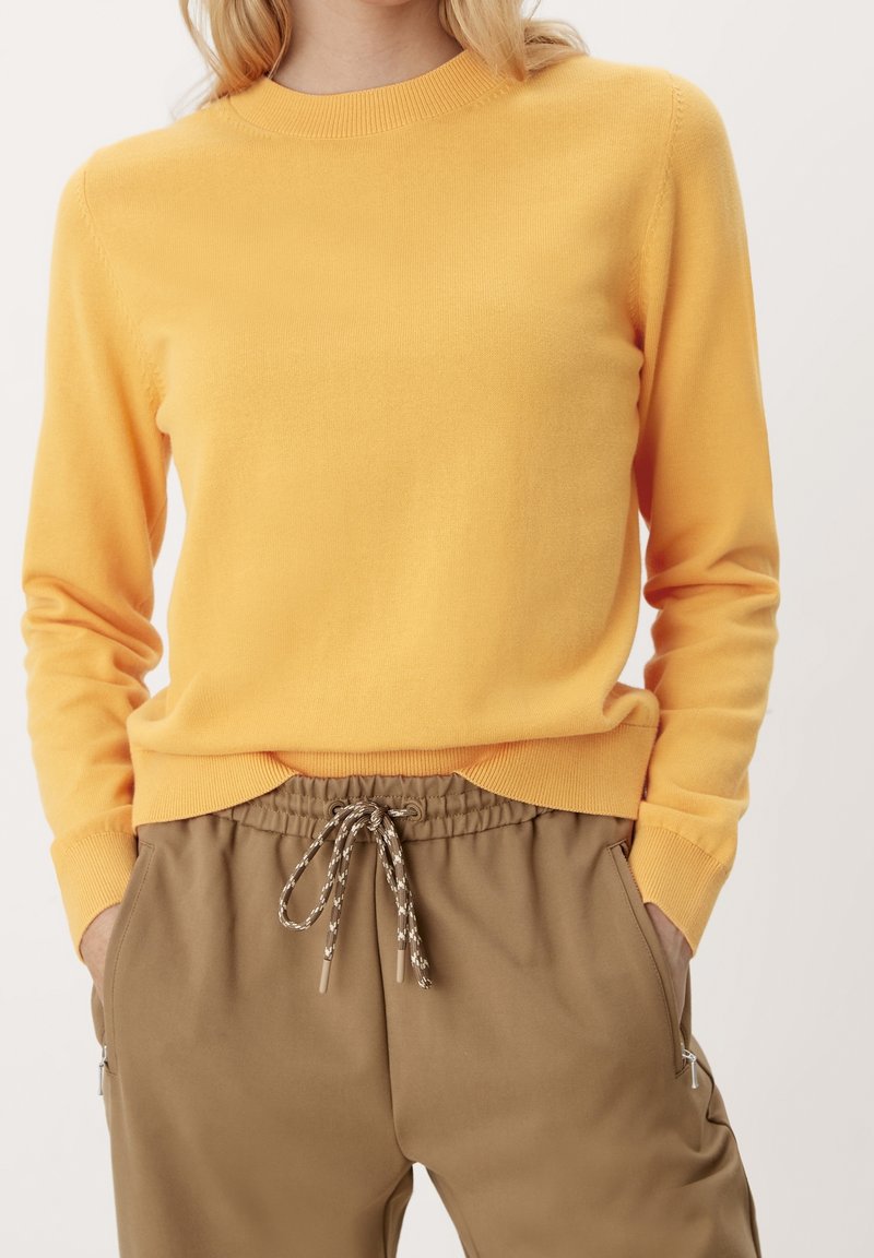 Gul strikket sweater med rund halsudskæring og lange ærmer, parret med brune tapered joggers med snor og sidelommer.